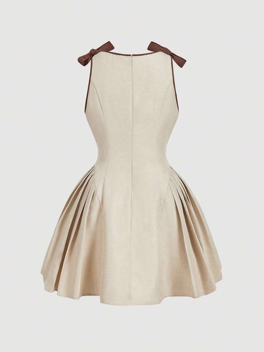 Mujer modelando un vestido mini color beige con lazos marrones en los hombros en una escalera de mármol.