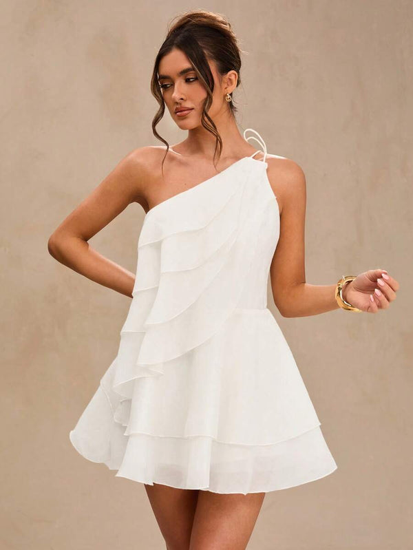 Detalle del diseño de volantes y escote asimétrico de un mini vestido blanco.