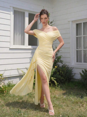 Vista de las piernas y el bajo de un vestido largo amarillo con abertura, mostrando sandalias blancas.