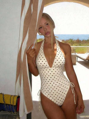 Mujer posando con un traje de baño entero color crema con lunares marrones y escote halter.