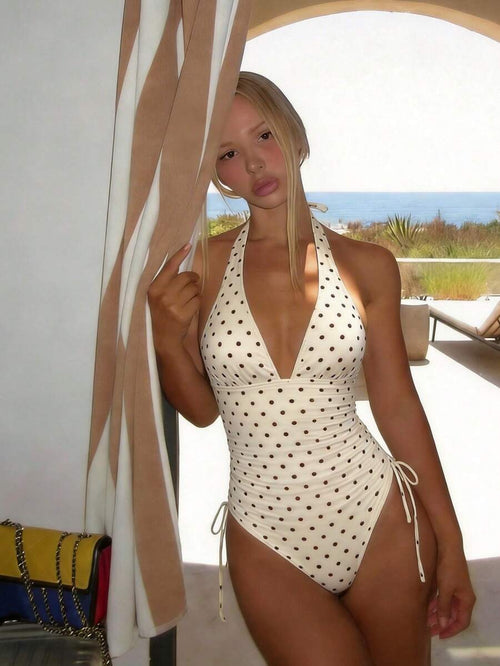 Mujer posando con un traje de baño entero color crema con lunares marrones y escote halter.