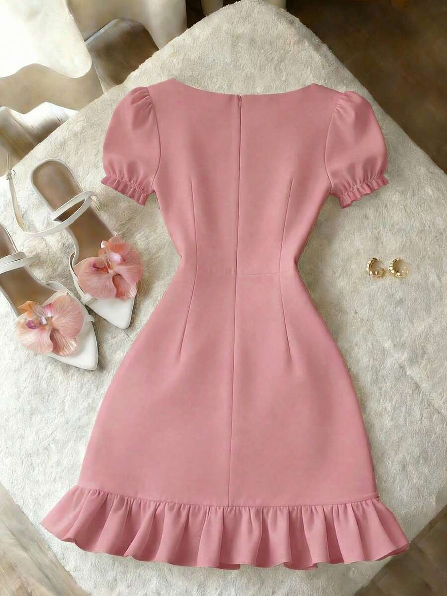 Vestido rosa corto de manga abullonada y escote cuadrado sobre un sofá gris.