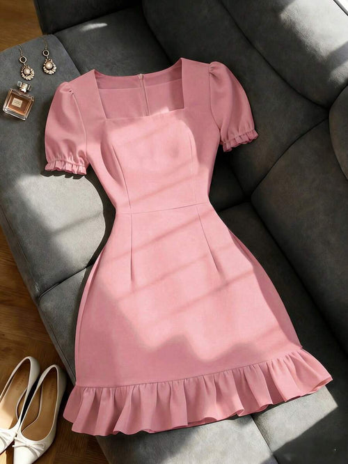 Vestido rosa corto de manga abullonada y escote cuadrado sobre un sofá gris.