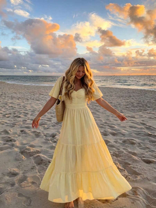 Mujer con vestido largo amarillo en la playa durante el atardecer.