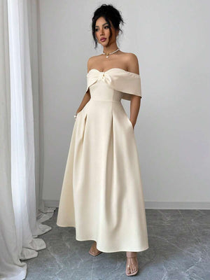 Mujer posando de lado con un vestido largo color crema, mostrando la silueta y el diseño de hombros caídos.