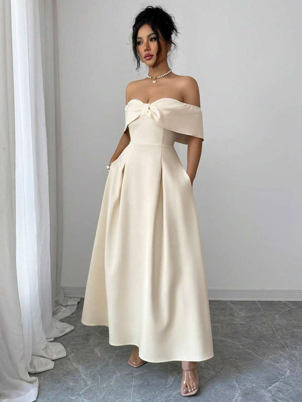 Mujer posando de lado con un vestido largo color crema, mostrando la silueta y el diseño de hombros caídos.