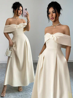 Vista frontal de una mujer con un vestido elegante color crema con hombros descubiertos y un lazo en el busto.