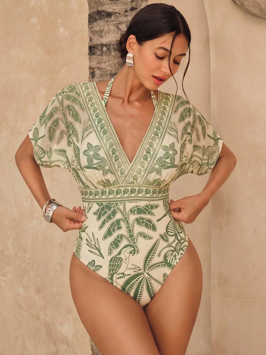 Mujer modelando traje de baño entero con estampado tropical verde y beige, con escote V profundo y mangas de mariposa.
