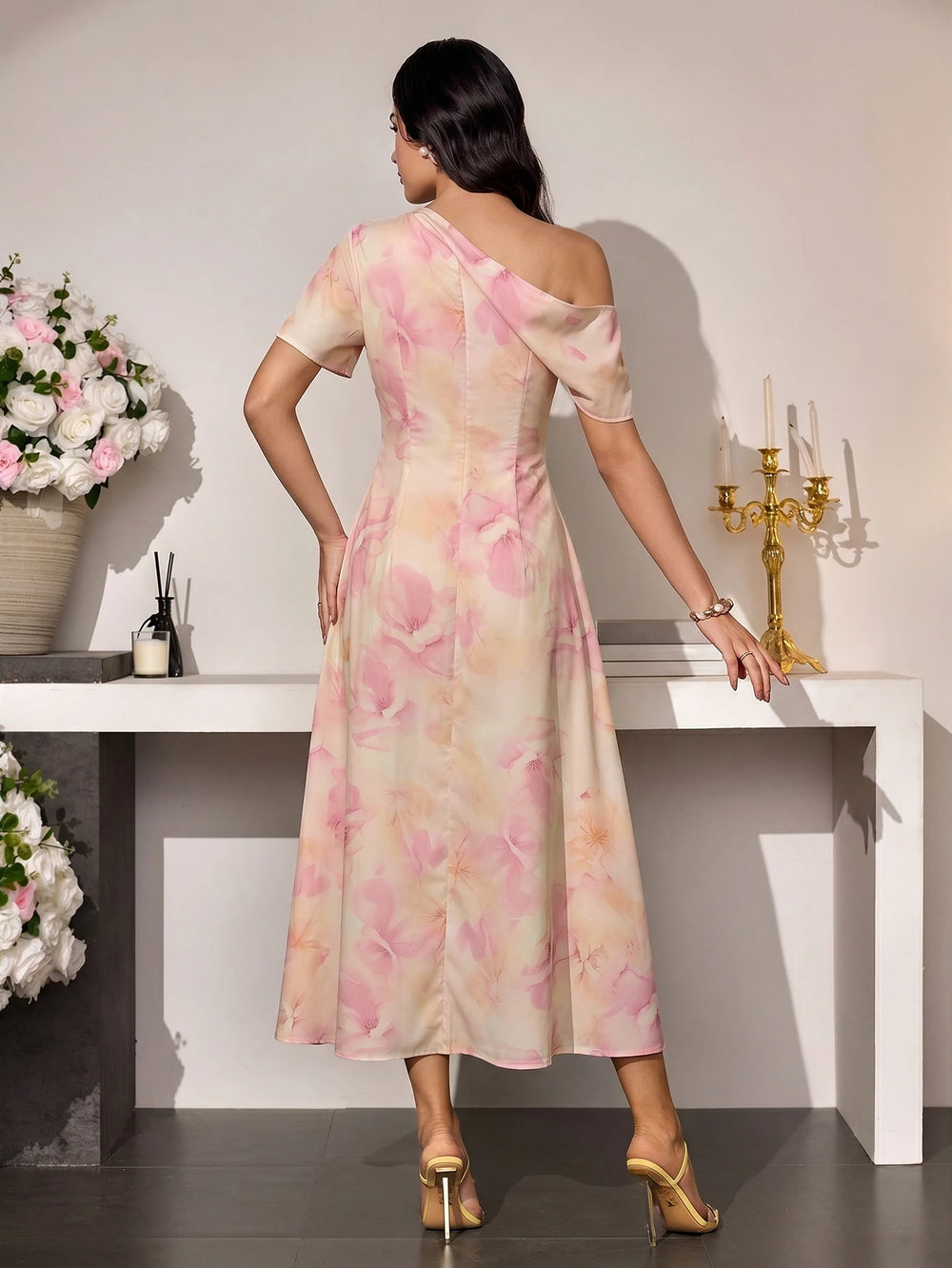 Mujer sentada luciendo un vestido floral rosa con escote asimétrico y un solo hombro.