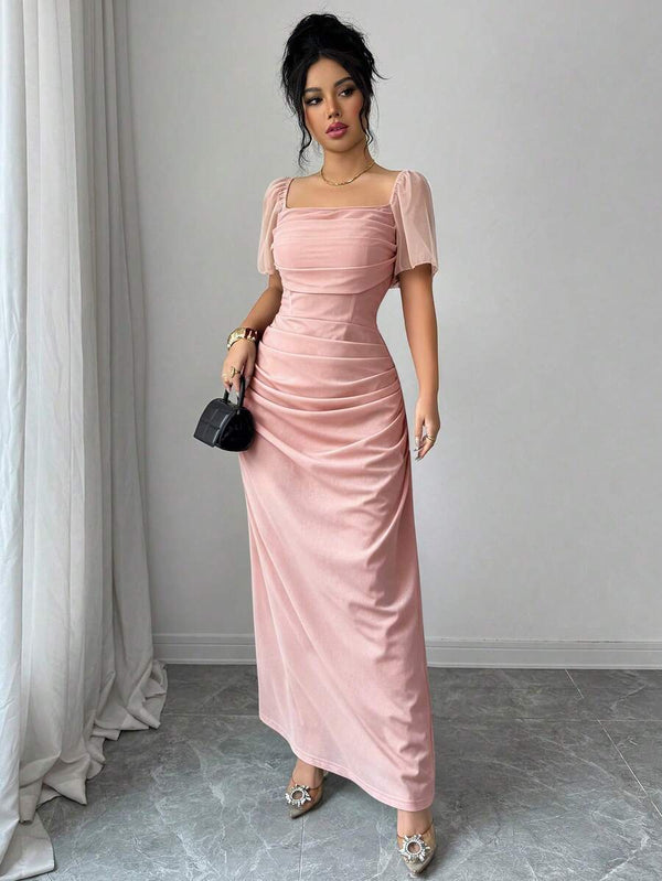 Modelo luciendo un vestido maxi elegante en tono rosa palo con diseño fruncido y corte A.
