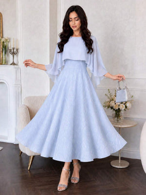 Mujer con vestido elegante azul cielo de largo midi y capa de gasa posando en una habitación.