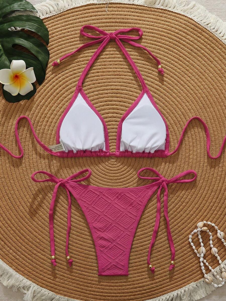 Bikini triangular color rosa fucsia con lazos ajustables visto desde arriba sobre una superficie de paja.