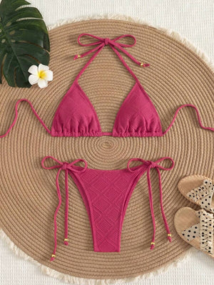 Bikini triangular color rosa fucsia con lazos ajustables visto desde arriba sobre una superficie de paja.