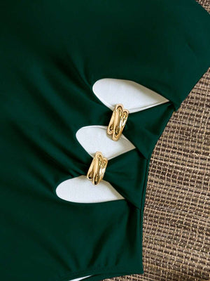 Primer plano de las aberturas laterales de un monokini verde, unidas por tres detalles de aros metálicos dorados.