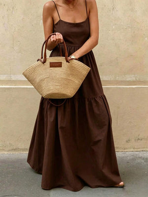 Mujer caminando con un vestido largo de verano color café mostrando el movimiento de la falda y un bolso de mano de fibra natural.
