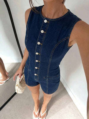 Primer plano del torso de una mujer con un romper de denim azul oscuro mostrando el escote redondo y los botones frontales.