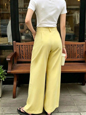 Detalle del pantalón amarillo de tiro alto con pinzas frontales y trabillas para cinturón.