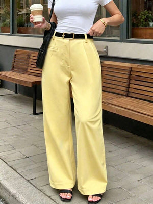 Mujer vistiendo un pantalón amarillo de pierna ancha con una blusa blanca y cinturón negro en la calle.