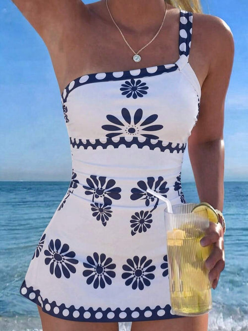Mujer luciendo un vestido corto asimétrico blanco con flores y lunares azules frente al mar.