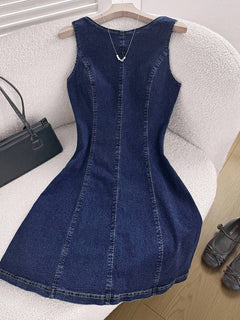 Vestido de mezclilla azul oscuro sin mangas con corte A, visto desde el frente sobre un sillón texturizado.
