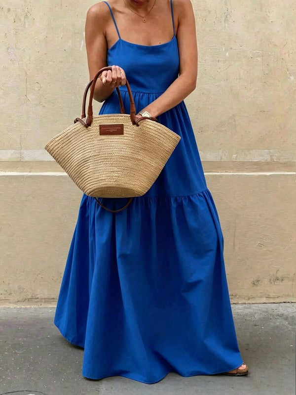 Mujer sosteniendo un bolso de paja mientras viste un vestido maxi azul con sandalias marrones.