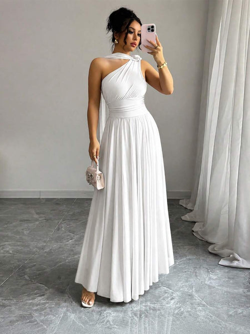 Mujer luciendo un vestido largo blanco de un hombro con detalle de nudo y falda plisada.