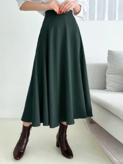 Falda midi acampanada en verde esmeralda combinada con una blusa blanca y botines marrones.