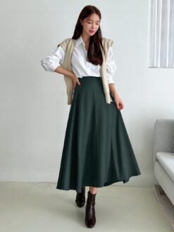 Falda midi acampanada en verde esmeralda combinada con una blusa blanca y botines marrones.