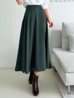 Falda midi acampanada en verde esmeralda combinada con una blusa blanca y botines marrones.