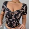 Modelo luciendo blusa crop floral negra con escote corazón y detalles de nudo.