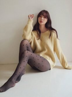 Modelo sentada luciendo medias negras con diseño de corazones.