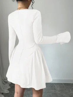 Mujer usando vestido corto blanco elegante con escote corazón y mangas largas.