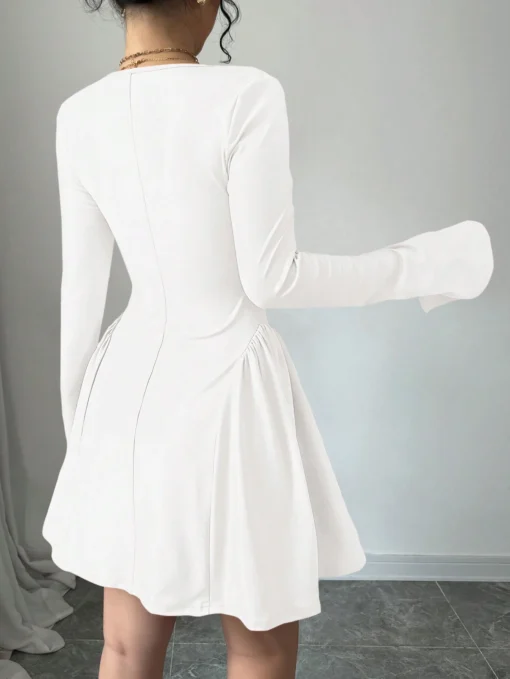 Mujer usando vestido corto blanco elegante con escote corazón y mangas largas.