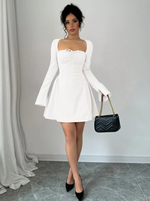 Mujer usando vestido corto blanco elegante con escote corazón y mangas largas.