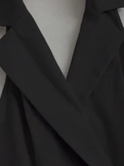 Detalle del cuello solapa del vestido corto negro con solapa y plisado.