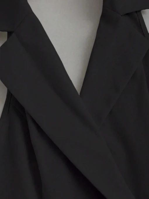 Detalle del cuello solapa del vestido corto negro con solapa y plisado.