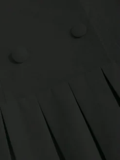 Detalle del plisado y doble botonadura del vestido corto negro con solapa y plisado.