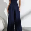 Mujer usando un mono largo azul marino sin tirantes y de talle alto, combinándolo con zapatillas blancas para un look casual.
