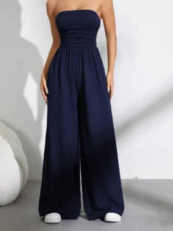 Mujer usando un mono largo azul marino sin tirantes y de talle alto, combinándolo con zapatillas blancas para un look casual.