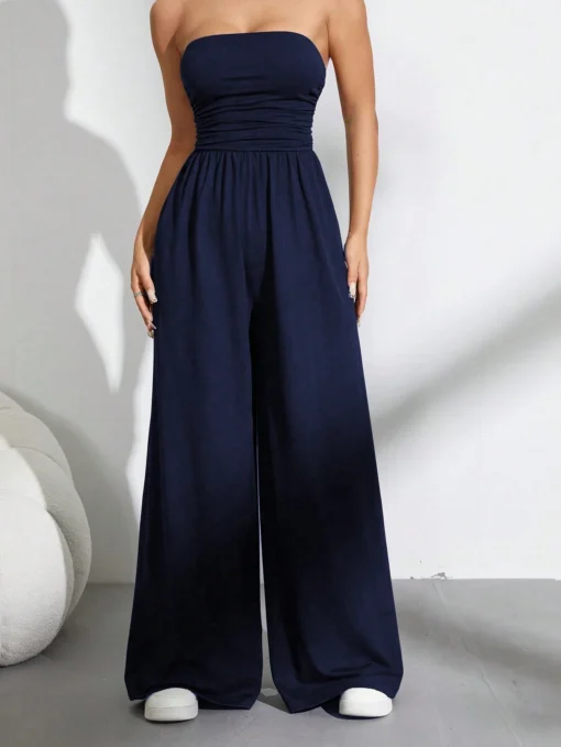 Mujer usando un mono largo azul marino sin tirantes y de talle alto, combinándolo con zapatillas blancas para un look casual.