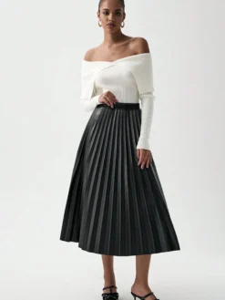 Modelo luciendo falda negra plisada con blusa blanca elegante.