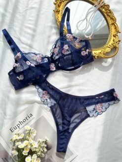 Set de lencería azul con bordado floral transparente sobre superficie blanca.