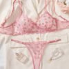 Set de lencería rosa con bordado floral transparente en fondo claro.