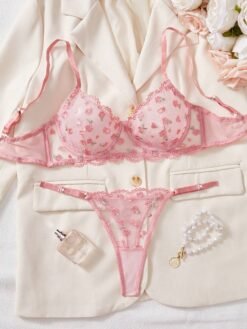 Set de lencería rosa con bordado floral transparente en fondo claro.