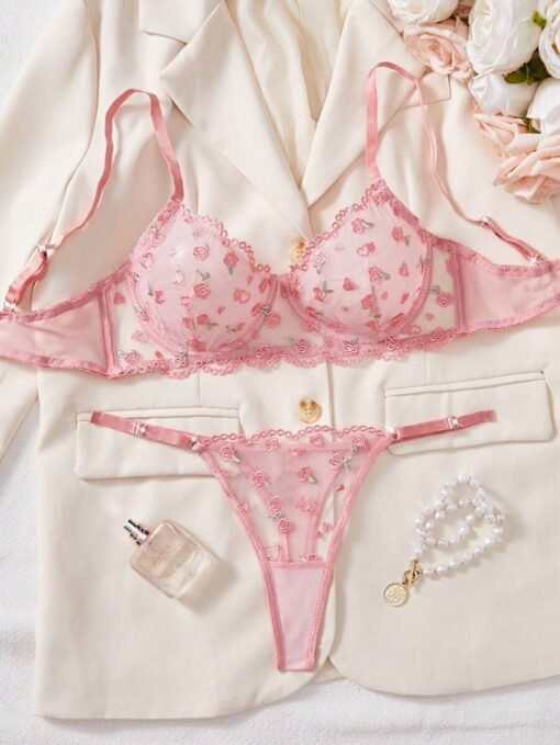 Set de lencería rosa con bordado floral transparente en fondo claro.
